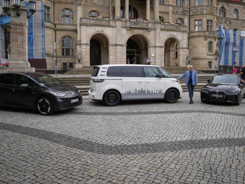 Drei Fahrzeuge stehen vor dem Neuen Rathaus. Ein Mann steht dazwischen.