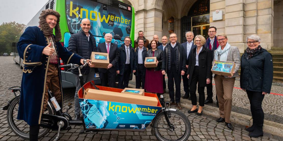 Menschengruppe mit Bus und Lastenrad. Auf dem Bus und dem Lastenrad steht "knowember".