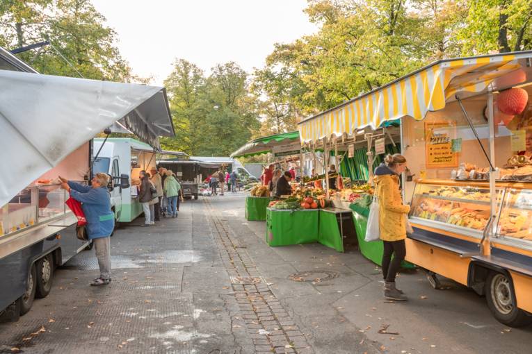 Menschen stehen an Wochenmarktwagen.