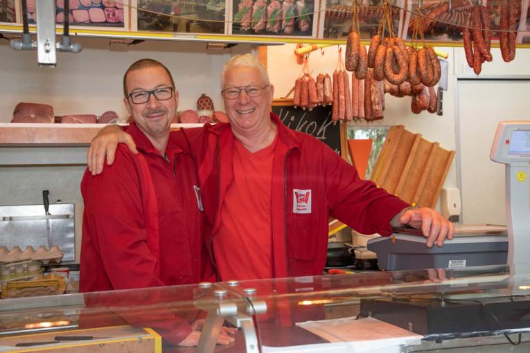 Zwei Männer lächeln in die Kamera. Einer hat einen Arm über die Schulter des anderen gelegt.